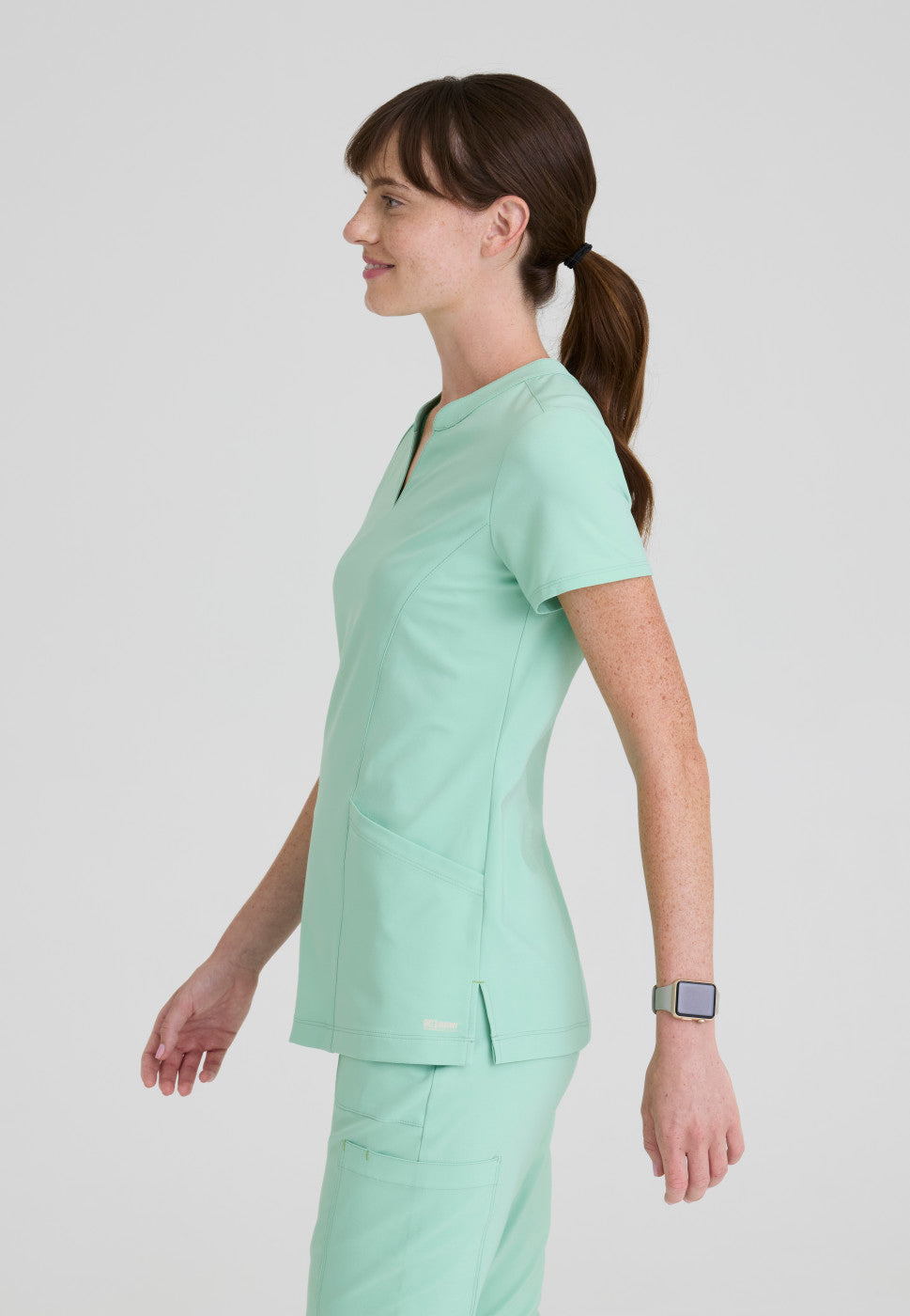 Side view of the GSST298 Grey's Anatomy Evolve Sky Banded Scrub Top in the colour Soft Melon.