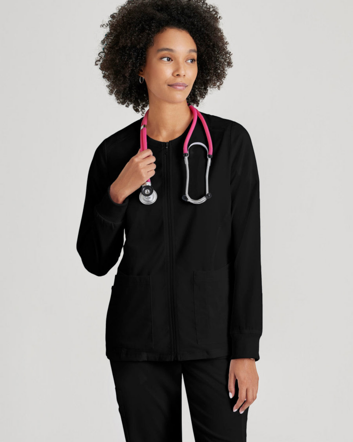Lasalle Uniform Gianna black zip-front scrub jacket with rib-knit cuffs worn by a model with a pink stethoscope.