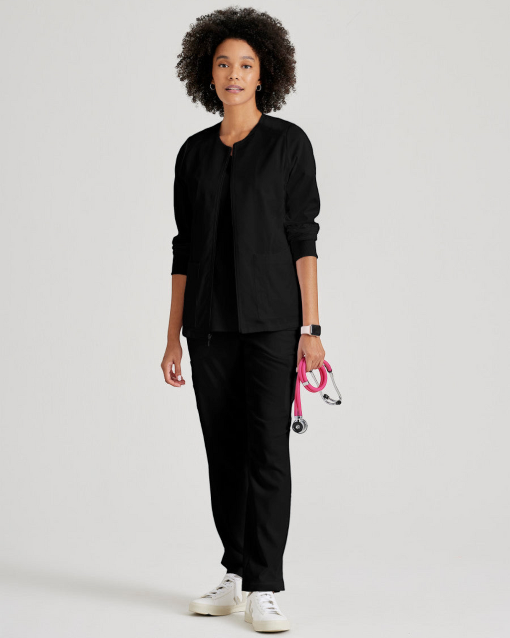 Model wearing a black Lasalle Uniform Gianna warm-up scrub jacket with a zip front and rib-knit cuffs.