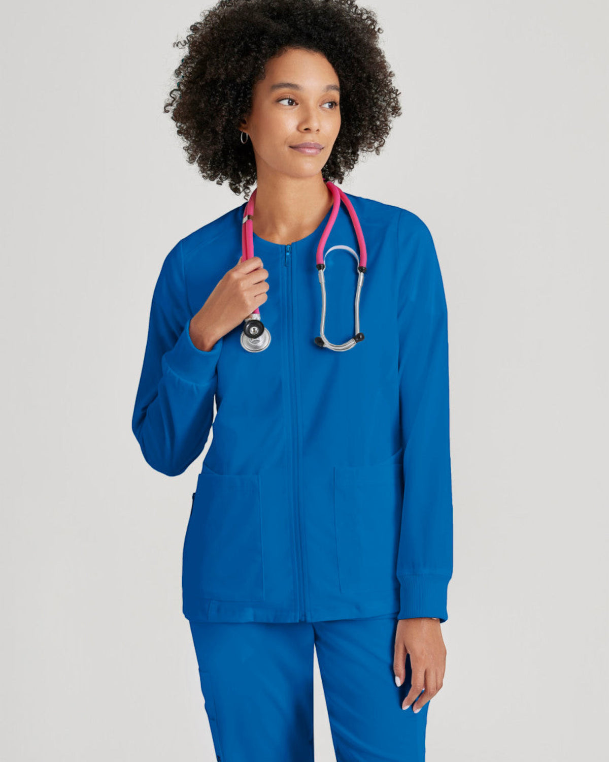 Lasalle Uniform model wearing a royal blue Grey's Anatomy by Barco Gianna zip-front scrub jacket with rib-knit cuffs.