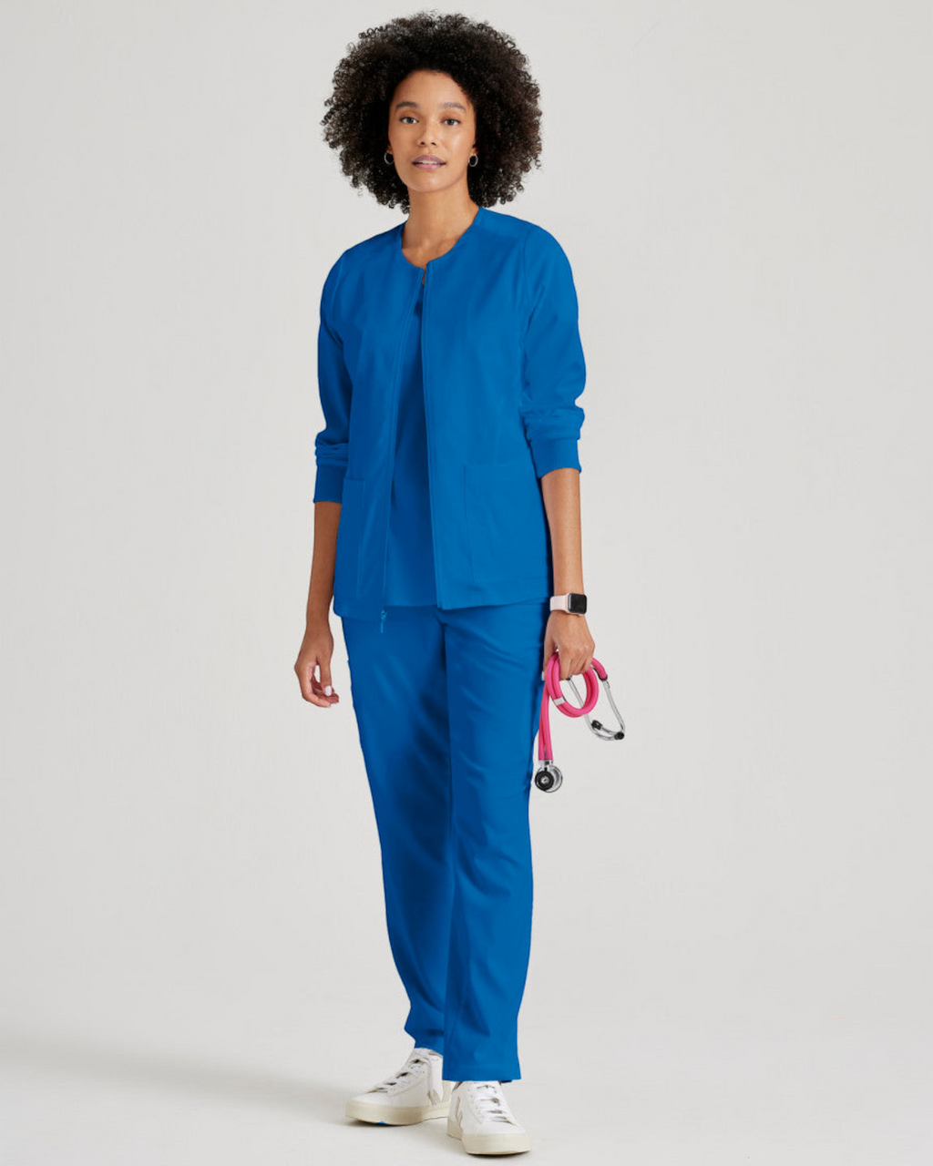 A model wearing a blue Lasalle Uniform Gianna warm-up scrub jacket with a round neck, zip front, and rib-knit cuffs.
