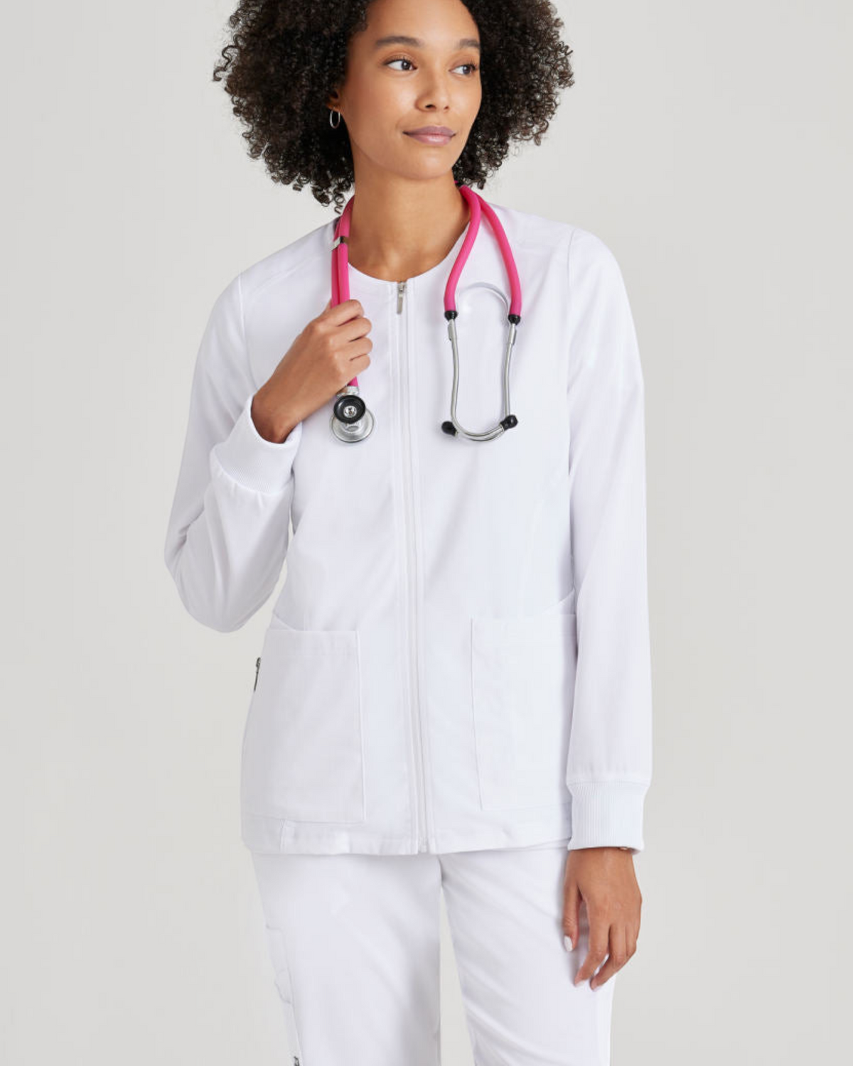 Lasalle Uniform Gianna white zip-front scrub jacket with rib-knit cuffs worn by a model with a pink stethoscope.