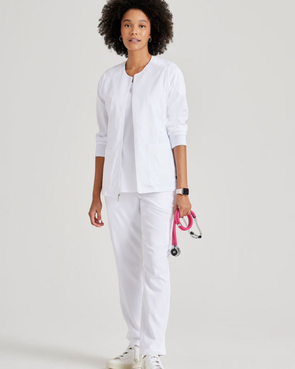 Lasalle Uniform Gianna white zip-front scrub jacket with rib-knit cuffs worn by a model with a pink stethoscope.