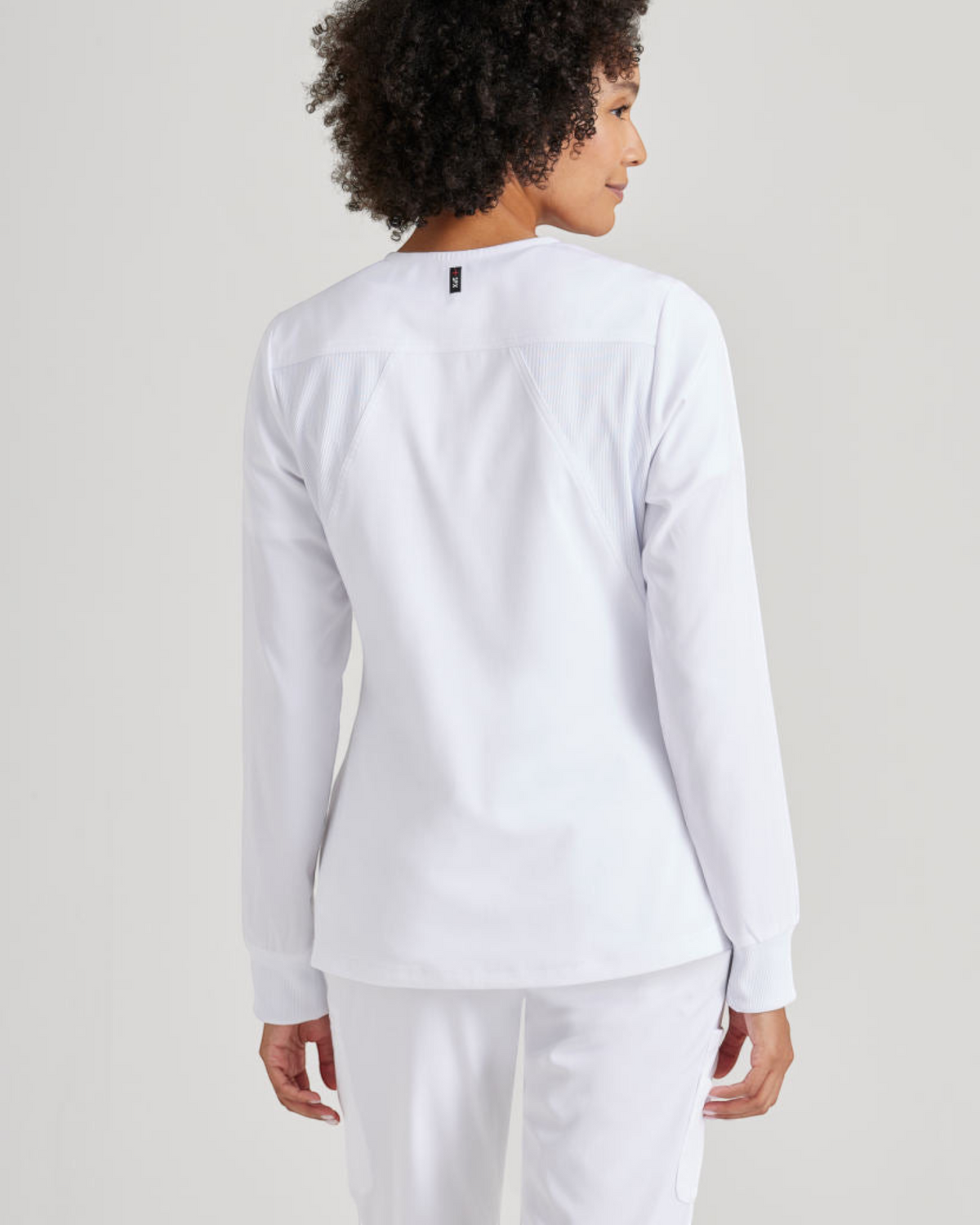 Back view of a woman wearing a white Lasalle Uniform Gianna scrub jacket with rib-knit cuffs and textured panels.