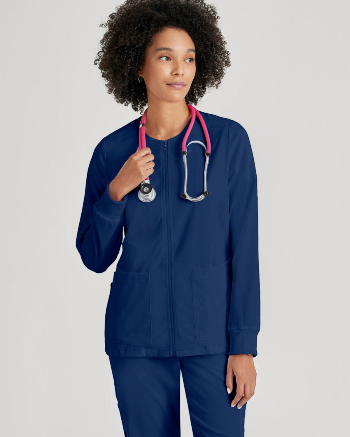 Lasalle Uniform Gianna navy blue zip-front scrub jacket with rib-knit cuffs worn by a model with a pink stethoscope.