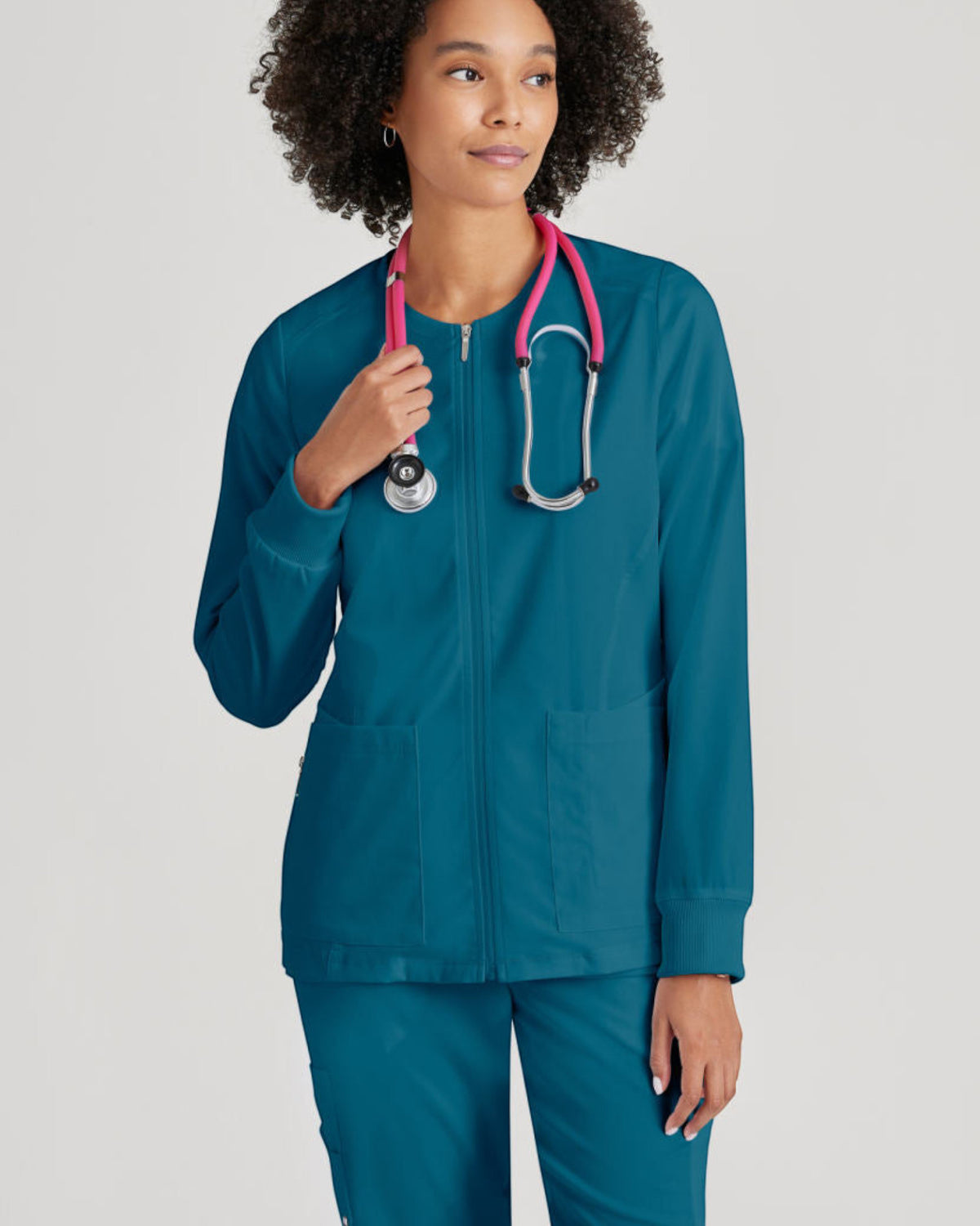 Lasalle Uniform Gianna warm-up scrub jacket in teal with a full zip front, rib-knit cuffs, and a stethoscope.