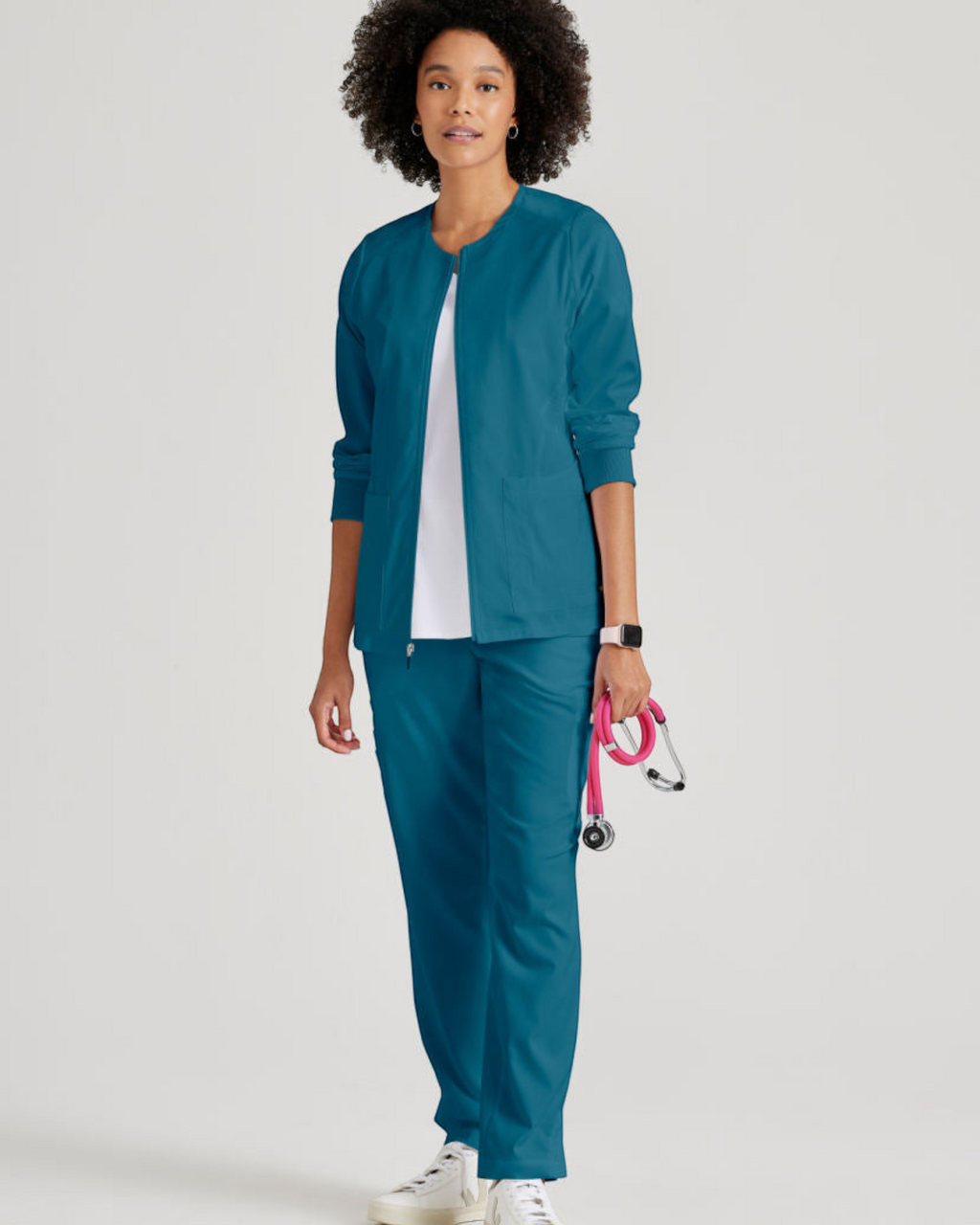 Model wearing a teal Grey's Anatomy by Barco Gianna warm-up scrub jacket from Lasalle Uniform with rib-knit cuffs.