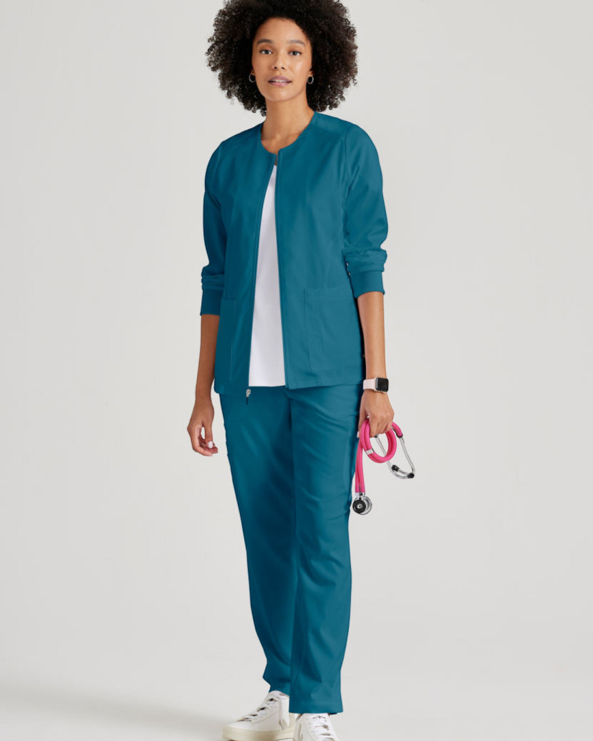 Model wearing a teal Grey's Anatomy by Barco Gianna warm-up scrub jacket from Lasalle Uniform with rib-knit cuffs.