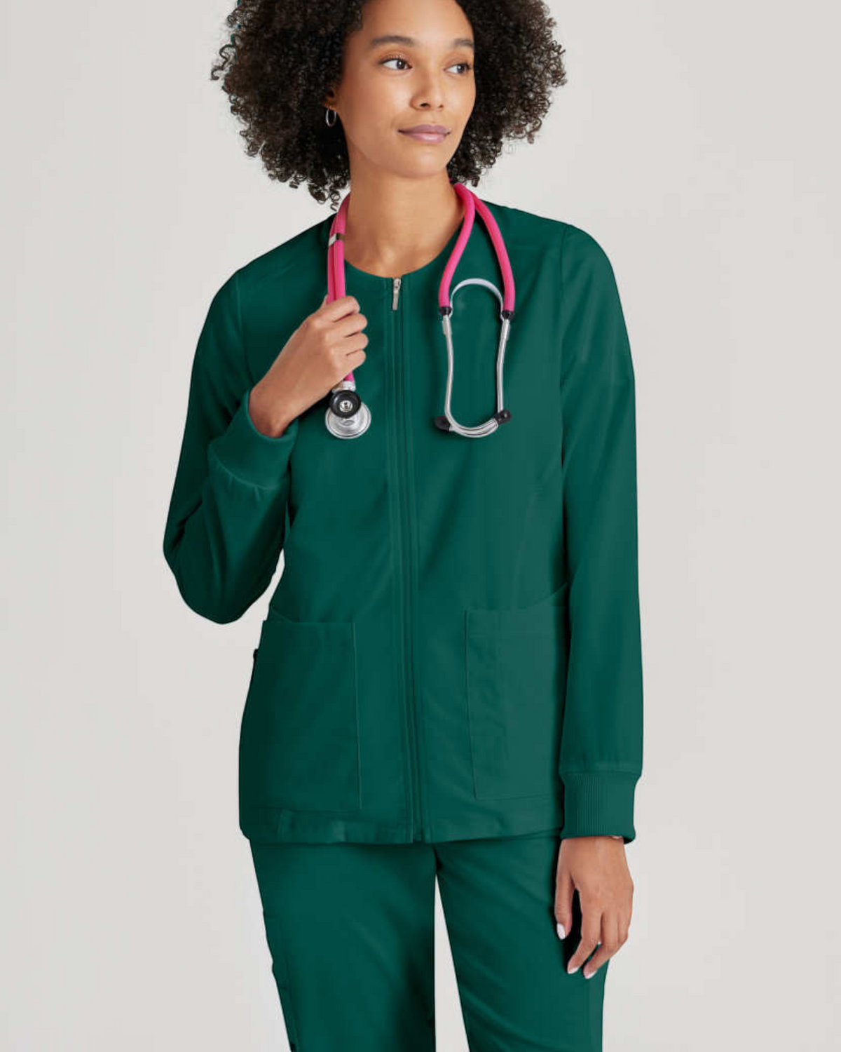 Lasalle Uniform Gianna warm-up scrub jacket in dark green with a full zip front, rib-knit cuffs, and a stethoscope.