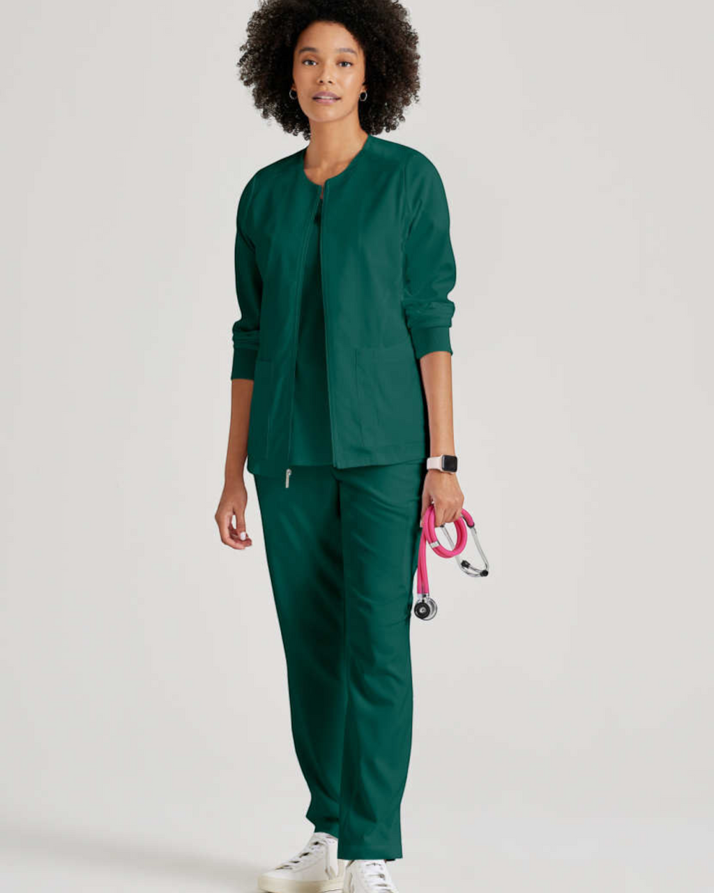 Lasalle Uniform model wearing a dark green Gianna zip-front scrub jacket with rib-knit cuffs and matching scrub pants.