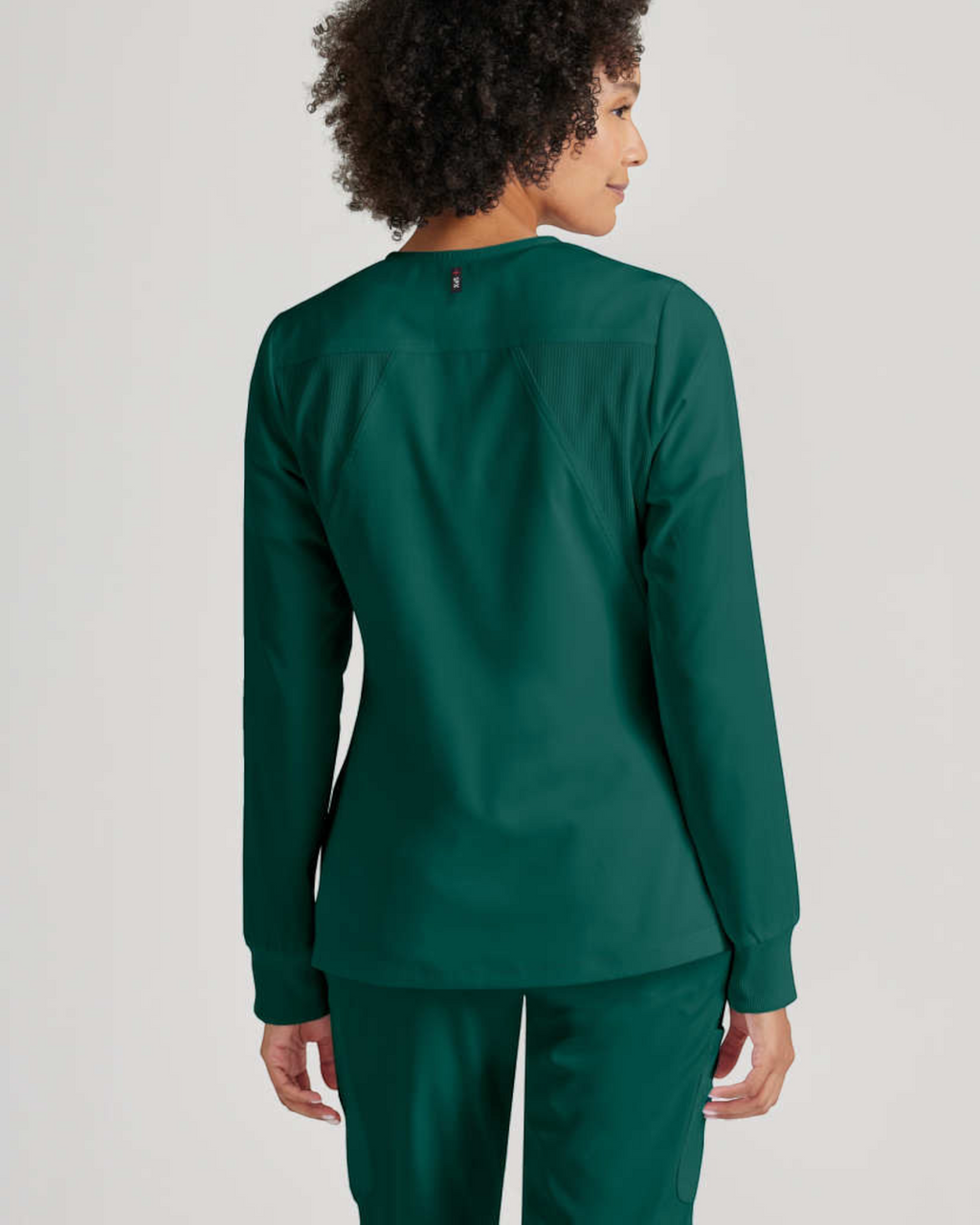 Back view of a woman wearing a dark green Lasalle Uniform Grey's Anatomy by Barco Gianna scrub jacket with rib-knit.