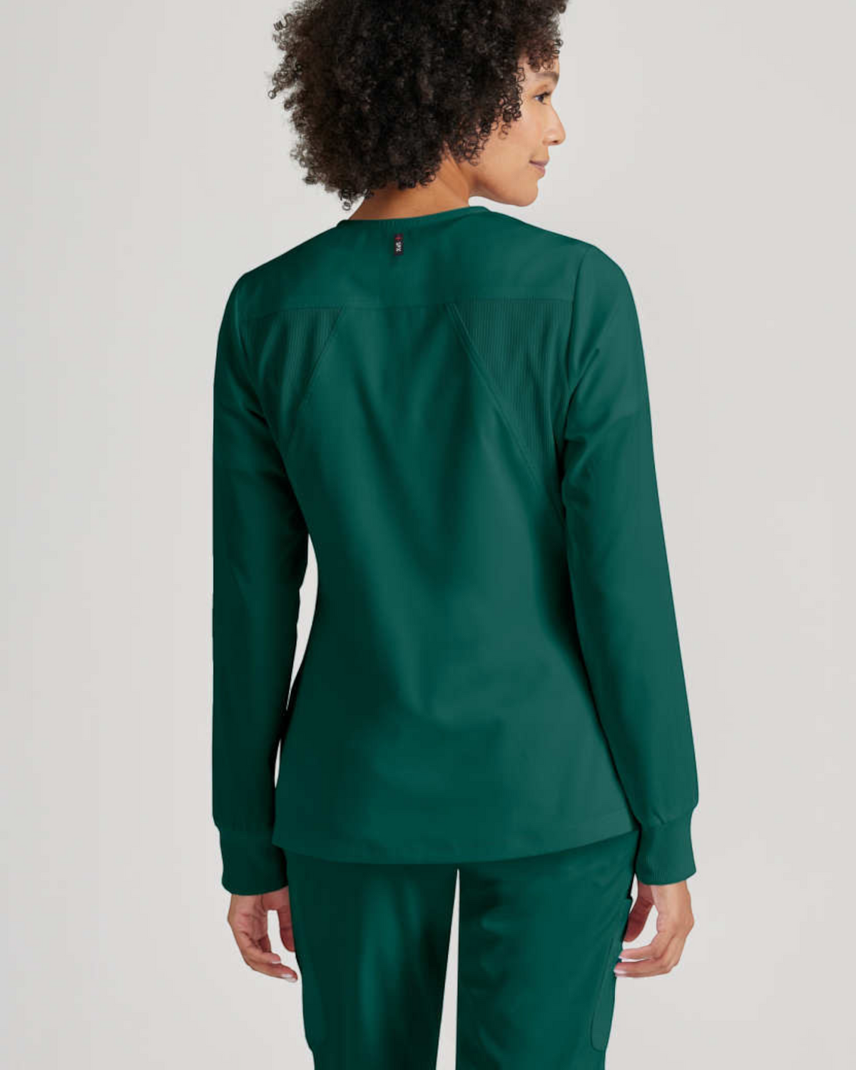 Back view of a woman wearing a dark green Lasalle Uniform Grey's Anatomy by Barco Gianna scrub jacket with rib-knit.