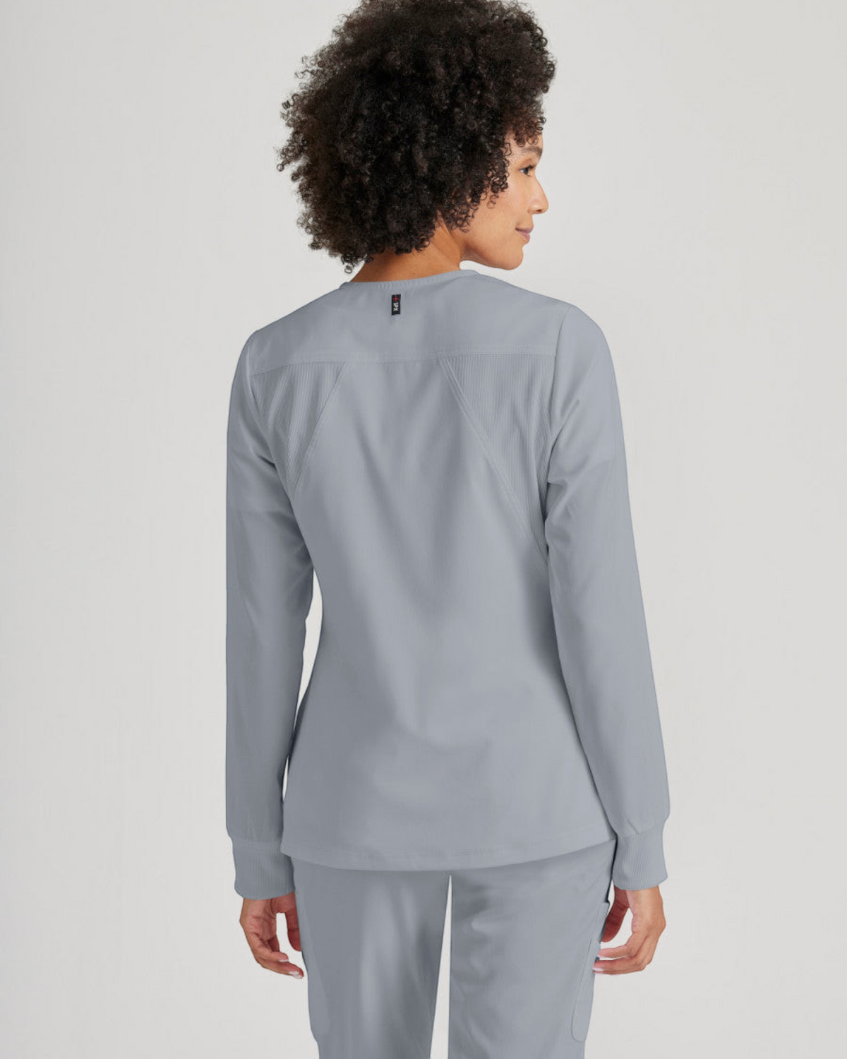 Back view of a woman wearing a grey Grey's Anatomy by Barco Gianna warm-up scrub jacket from Lasalle Uniform