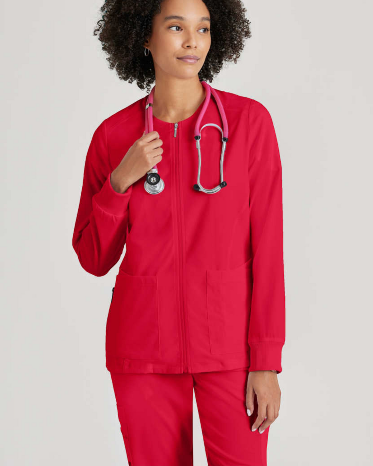 Lasalle Uniform Gianna warm-up scrub jacket in red with a round neck, zip front, and rib-knit cuffs worn by a model.