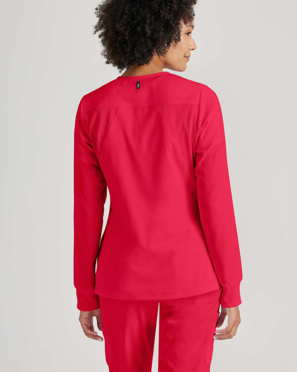 Back view of a woman wearing a bright pink Lasalle Uniform Gianna warm-up scrub jacket with rib-knit back panels.