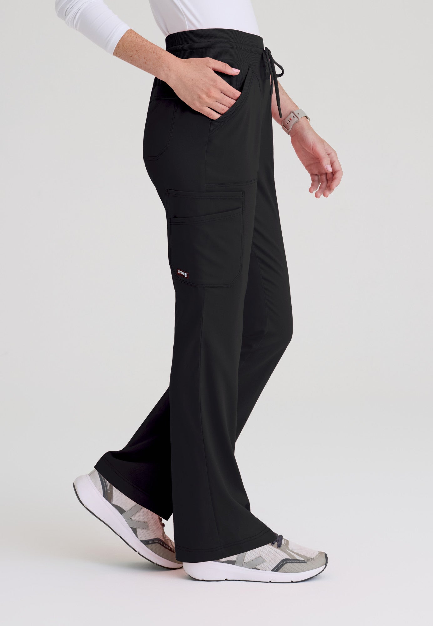 Side view of Kristi scrub pant showing deep cargo pockets and flared leg silhouette on soft stretch fabric. Black colour.