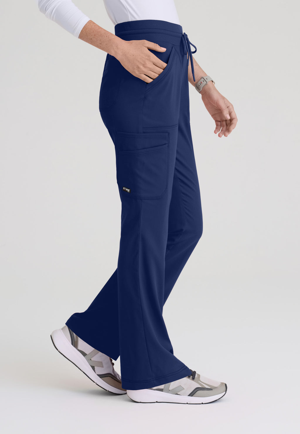 Side view of Kristi scrub pant showing deep cargo pockets and flared leg silhouette on soft stretch fabric. Indigo colour.