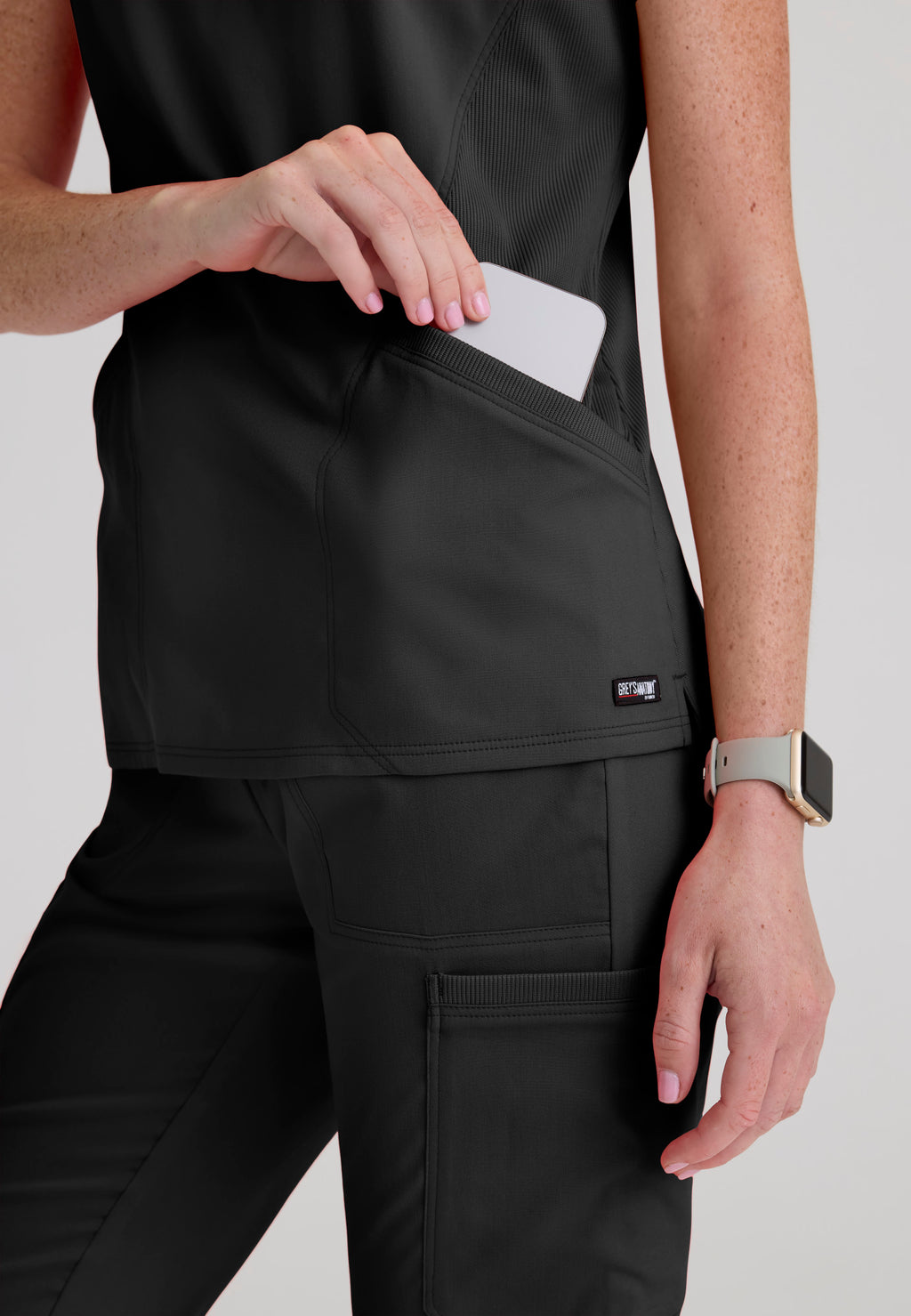 Close-up detail of the sleek zipper and rib-knit collar placket on soft antimicrobial scrub fabric.  Grey's Anatomy Kristi scrub top. Black colour.