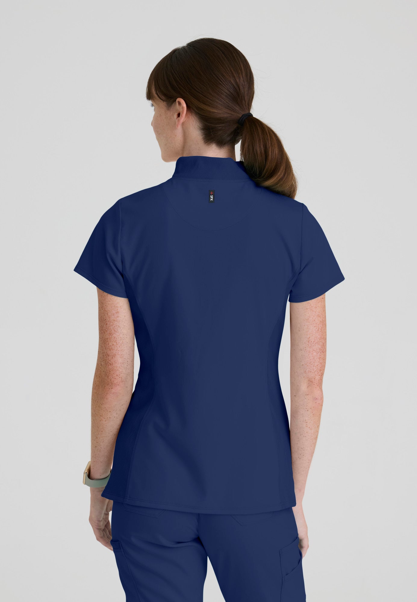 Back view of Grey's Anatomy Kristi scrub top highlighting the curved high-low hemline that provides added coverage while bending.  Indigo colour.