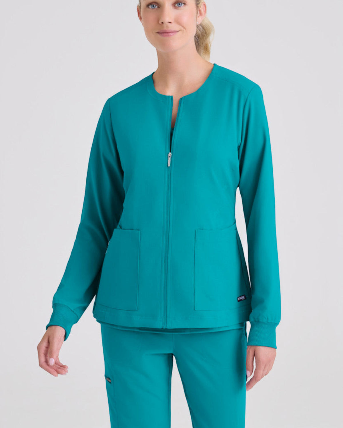 Lasalle Uniform Gianna warm-up scrub jacket in teal with a round neck, zip-front, and rib-knit cuffs on a model.