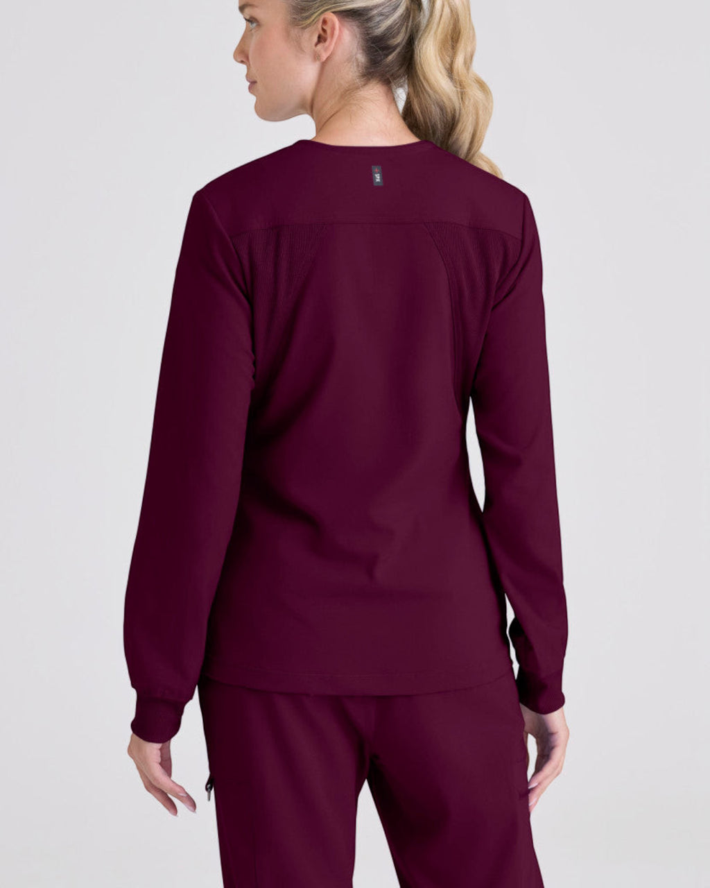Back view of a woman wearing a burgundy Grey's Anatomy by Barco Gianna warm-up scrub jacket from Lasalle Uniform