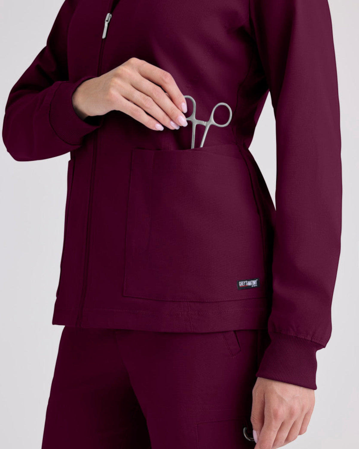 Lasalle Uniform Gianna scrub jacket in burgundy with a zip-front, rib-knit cuffs, and a pocket holding medical shears.