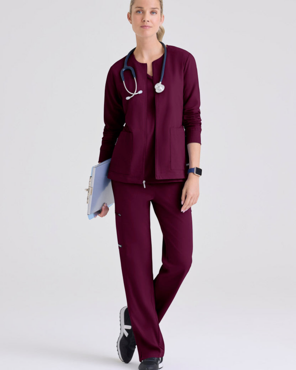 Lasalle Uniform model wearing a burgundy Grey's Anatomy by Barco Gianna warm-up scrub jacket with a stethoscope.