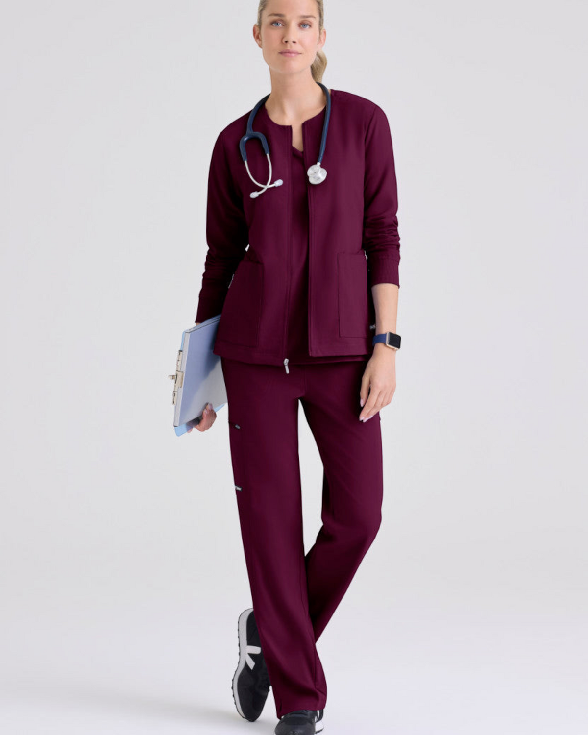 Lasalle Uniform model wearing a burgundy Grey's Anatomy by Barco Gianna warm-up scrub jacket with a stethoscope.