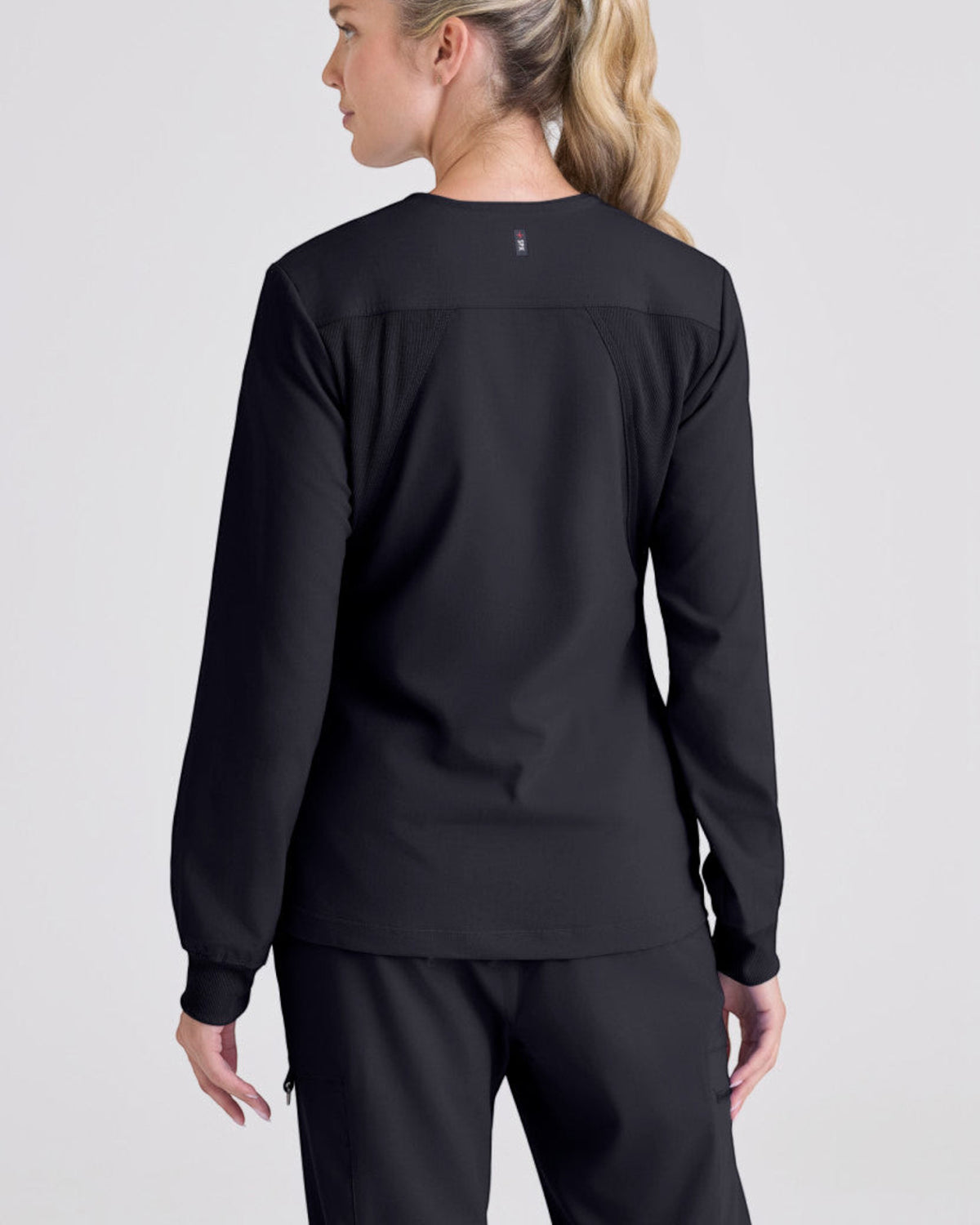 Back view of a woman wearing a black Lasalle Uniform Gianna warm-up scrub jacket with rib-knit cuffs and stretch fabric