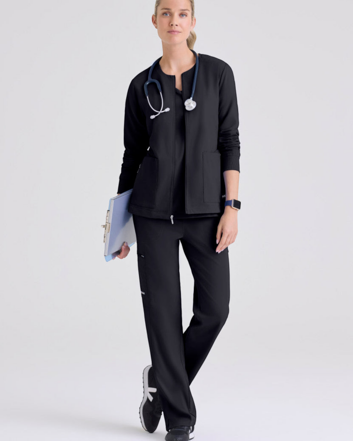 Lasalle Uniform model wearing a black Gianna warm-up scrub jacket with a zip front, rib-knit cuffs, and pockets.
